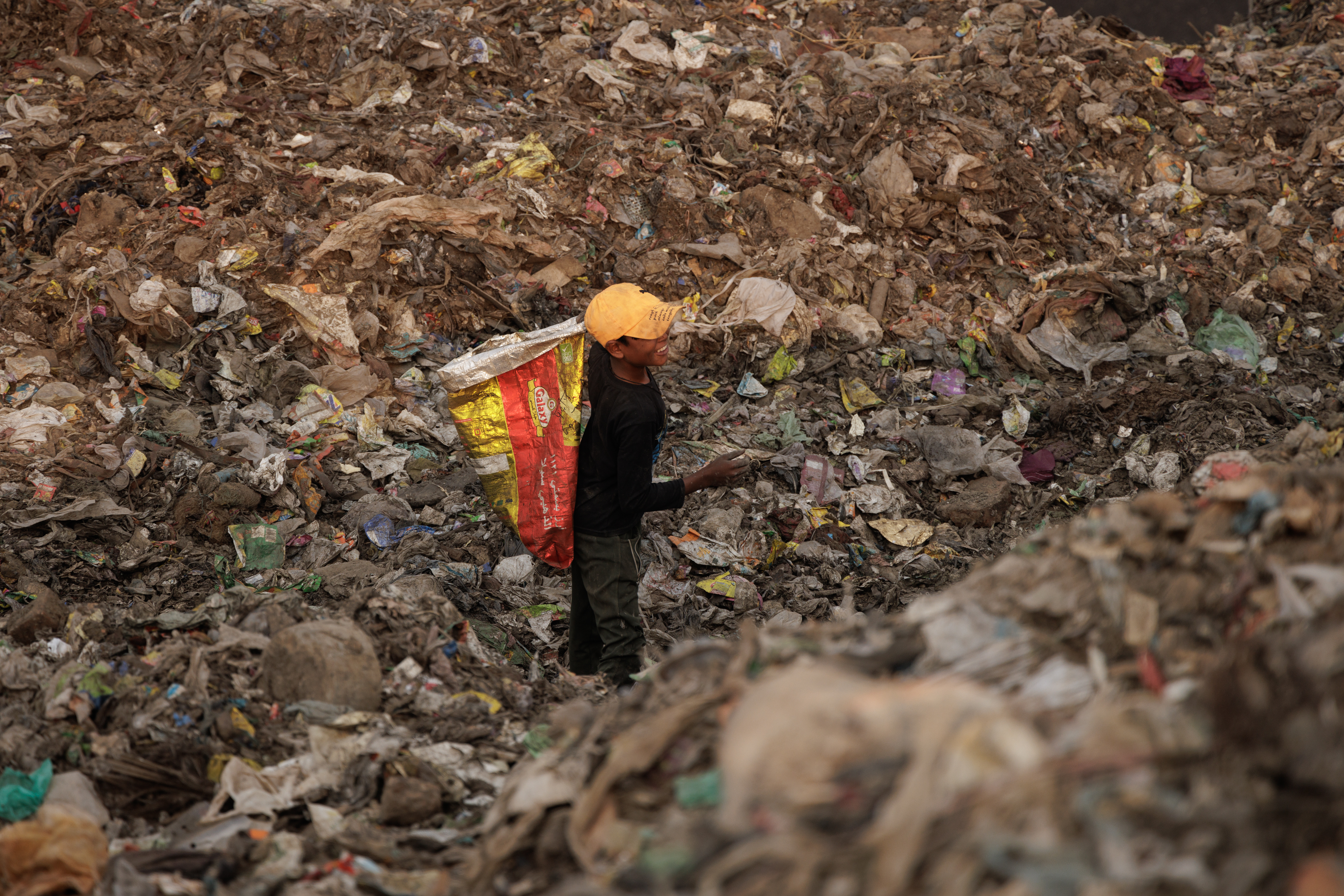 Boy in orange cap picking recyclables from the waste