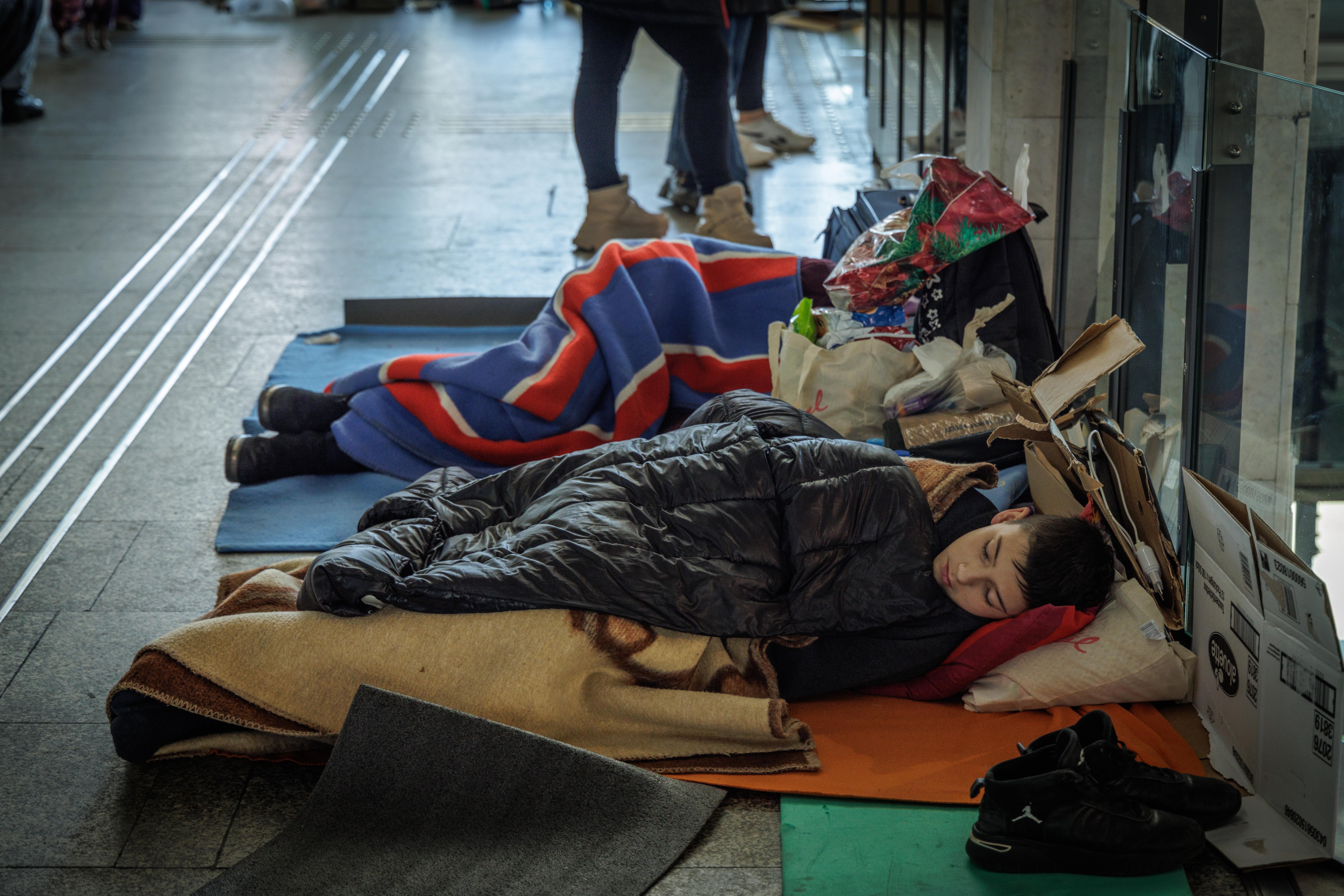 Boy sleeping on the floor of a train station wrapped in a coat