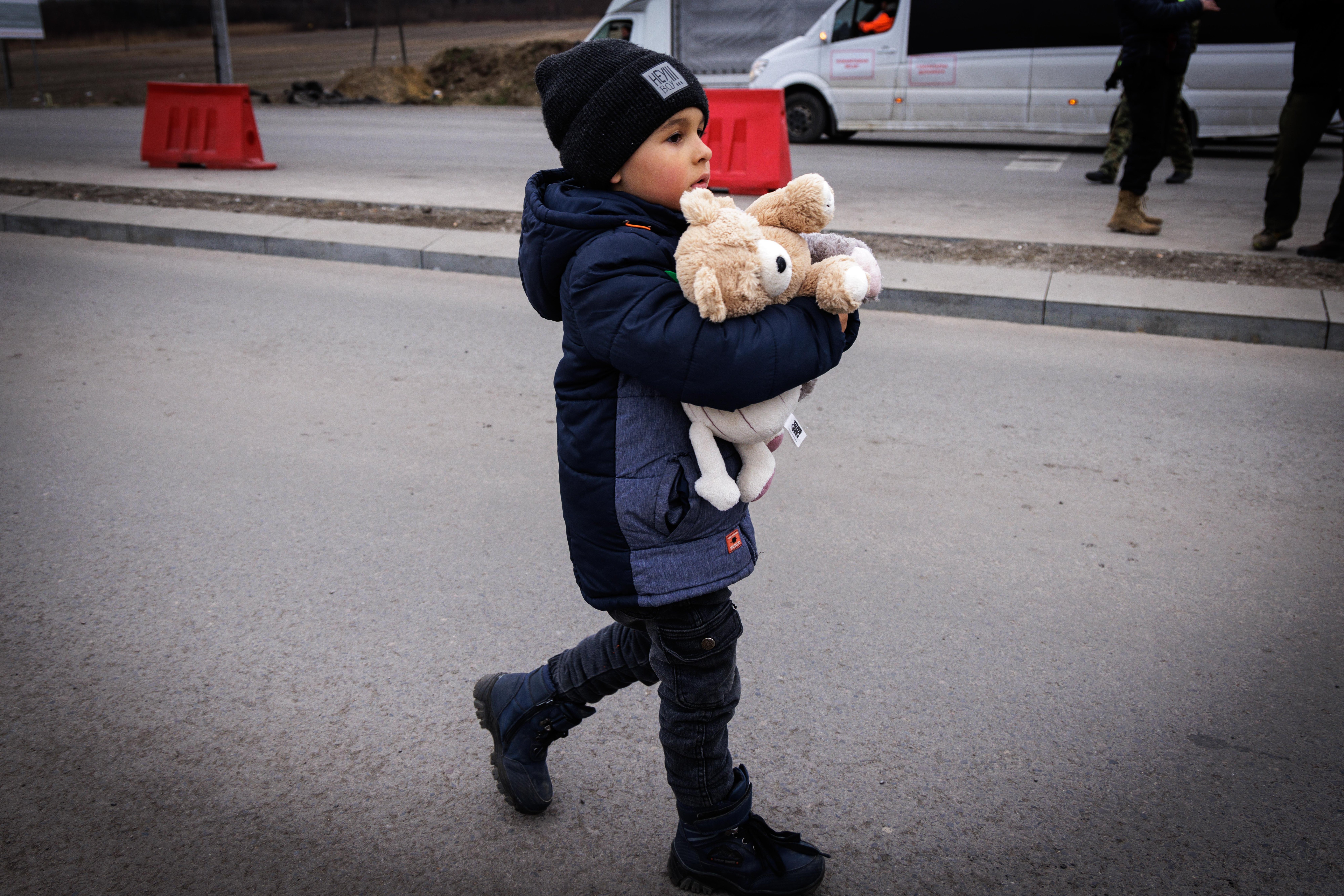 Boy walking alone across the border holding stuffed animals