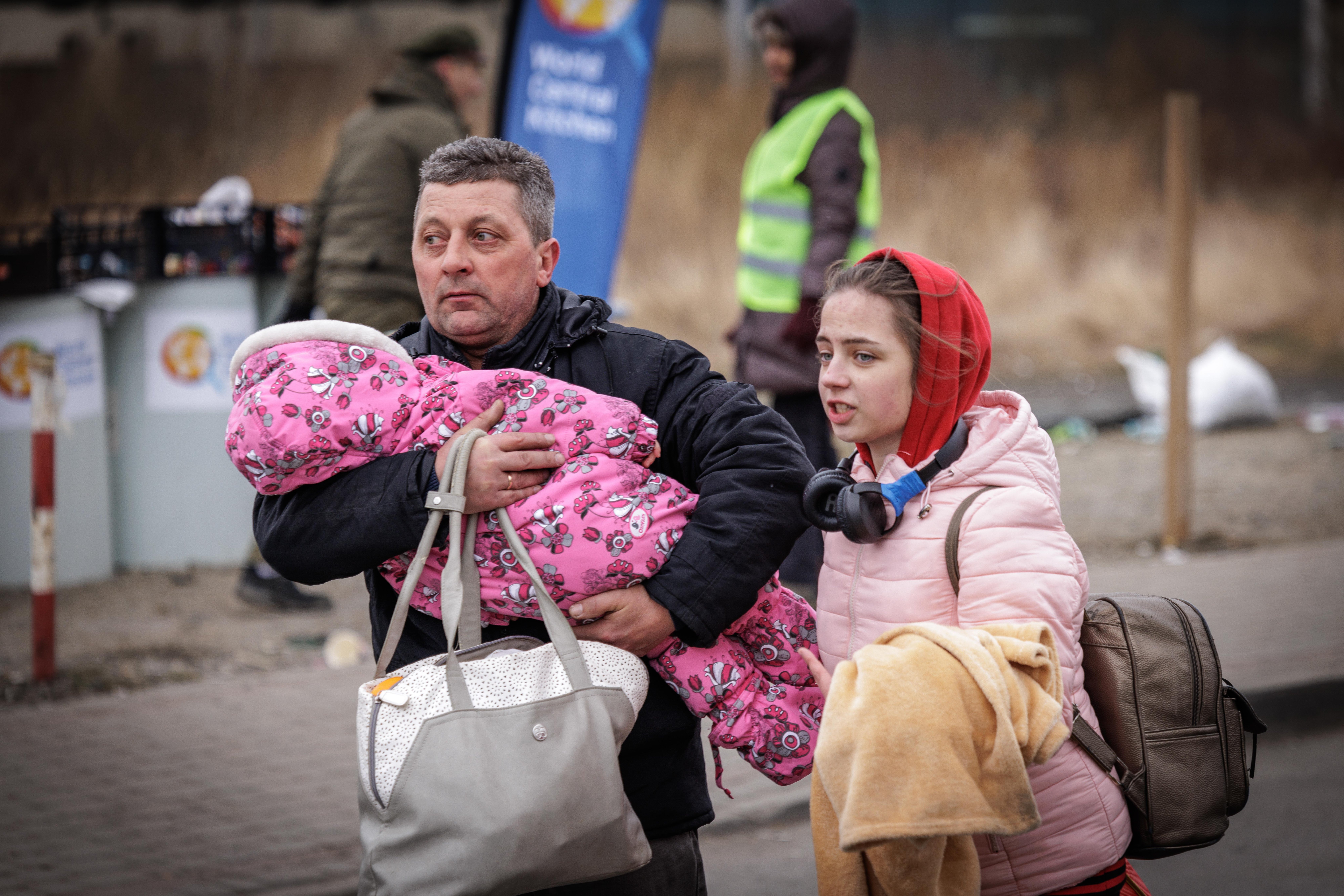 Father carrying infant in pink snowsuit with daughter