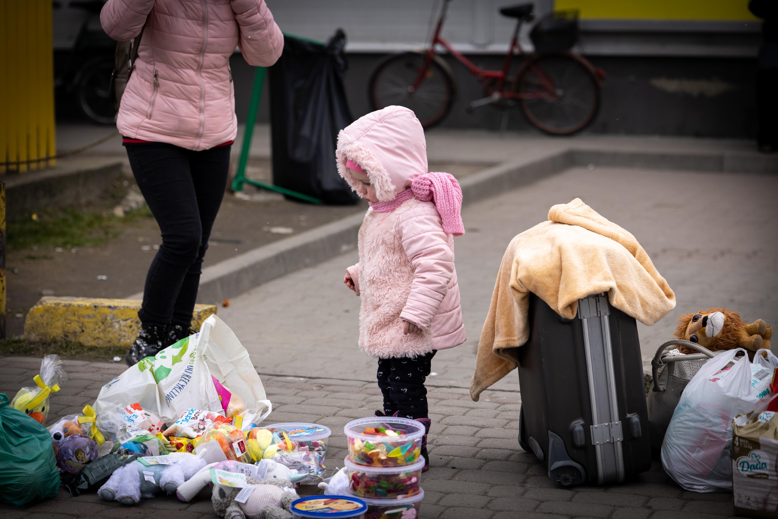 Toddler in pink coat looking at donated toys next to a suitcase